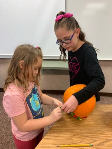 5th grader helping a kindergartener measure the pumpkins circumference.